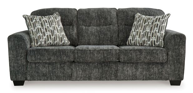 A three-seat sofa is presented in a gray-charcoal fabric with a textured, slightly mottled appearance.  The upholstery has a subtle pattern giving a variation in the shade throughout.  Three matching accent pillows, featuring a pattern of vertical stripes and light beige/cream tones against a darker gray background, are placed on the seat cushions. The sofa has gently curved armrests and dark-colored, faux-wood finish legs. The sofa is presented against a plain white background, which helps to highlight the sofa's color and texture.